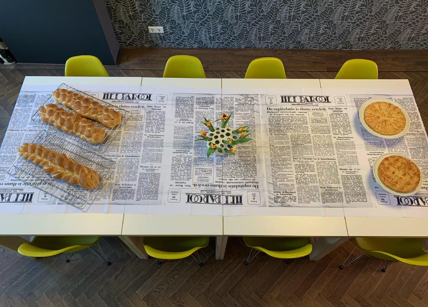 Gedekte tafel met krantenkleed van Het Parool, gevlochten broden en taarten