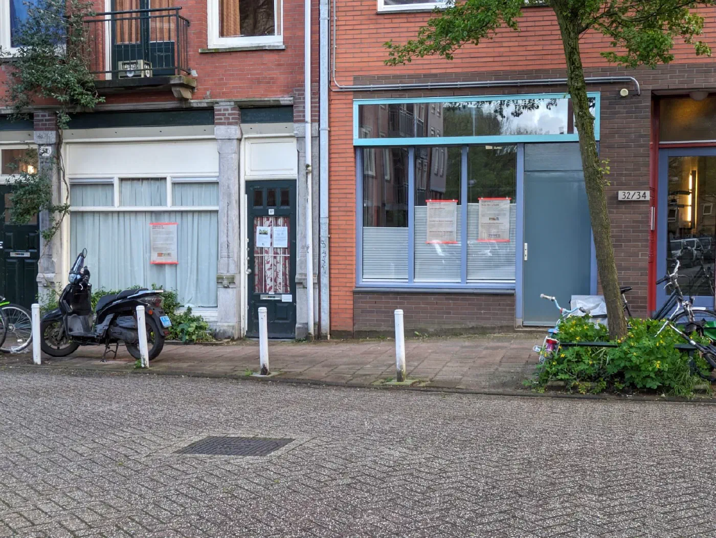 Gedenkposters achter de ramen van twee panden in een straat in de Oosterparkbuurt