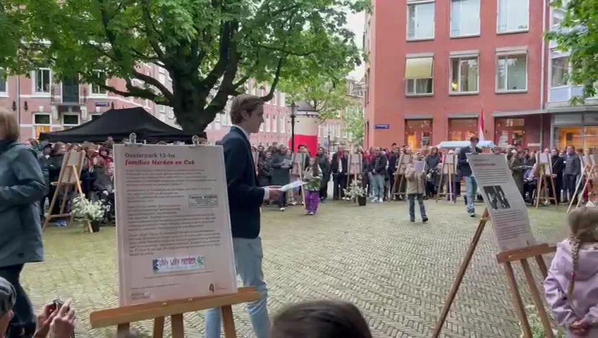 Jonge spreker leest voor tussen gedenkposters op ezels, omringd door publiek