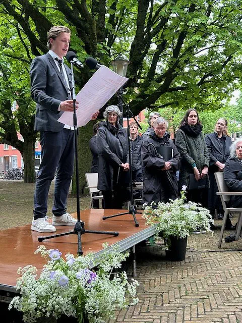 Jonge man in pak leest een tekst voor achter een microfoon op het podium