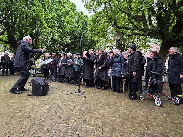 Dirigent leidt een koor van oudere zangers onder de bomen op het plein