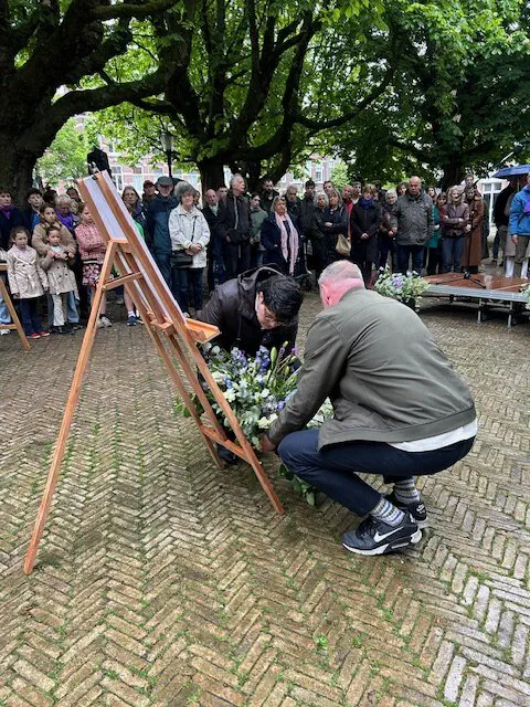 Twee mannen leggen een bloemstuk bij een ezel met gedenkposter