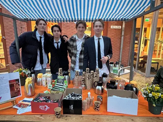 Vier jongemannen in pak achter een tafel met koffie en thee onder een luifel