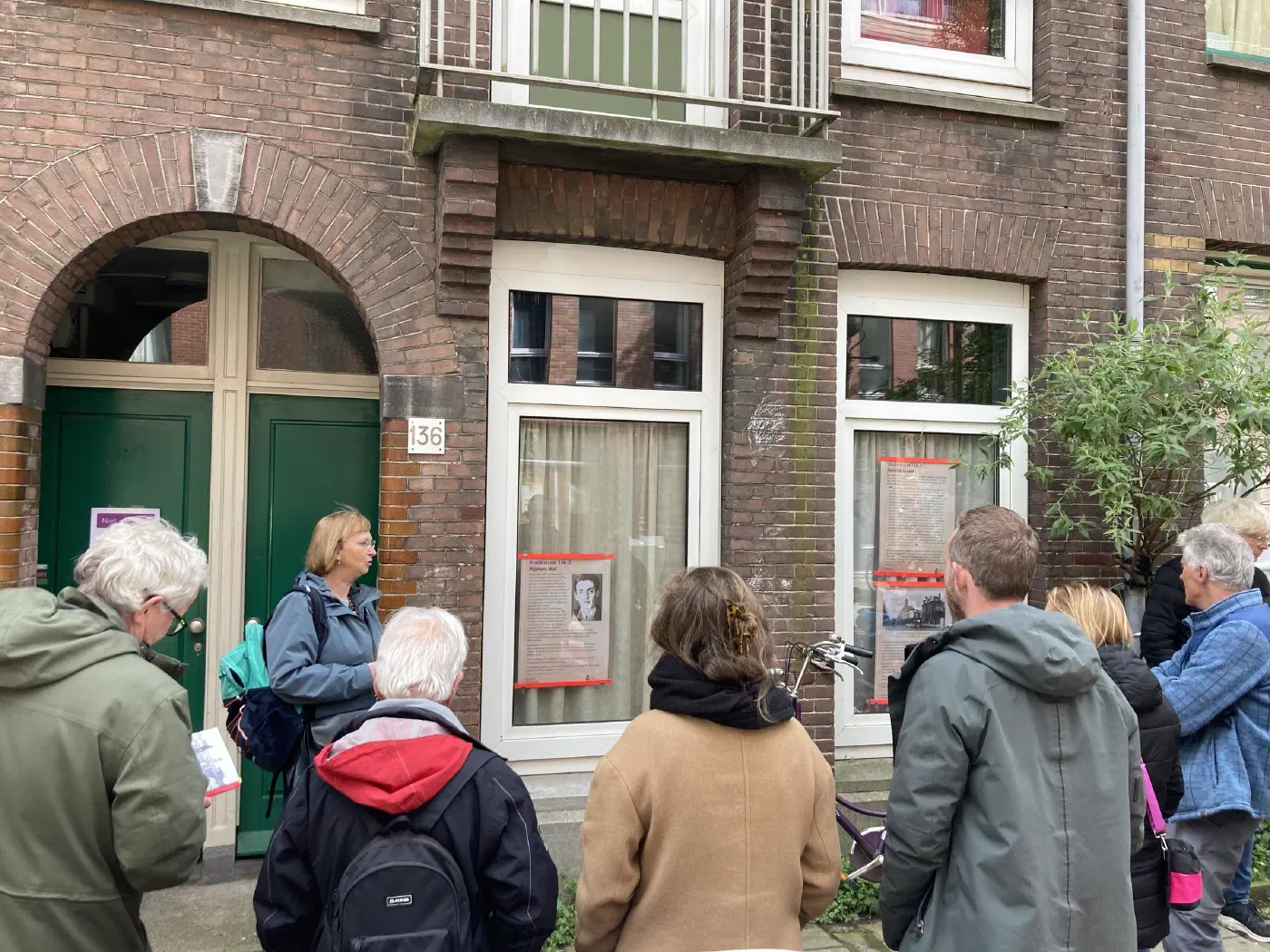 Deelnemers luisteren naar een gids voor de gedenkposters bij Vrolikstraat 136
