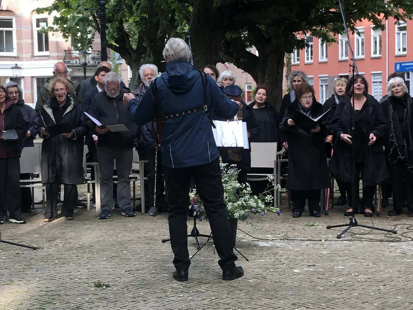 Jiddisj koor Hejmisj Zain zingt onder leiding van een dirigent onder de bomen