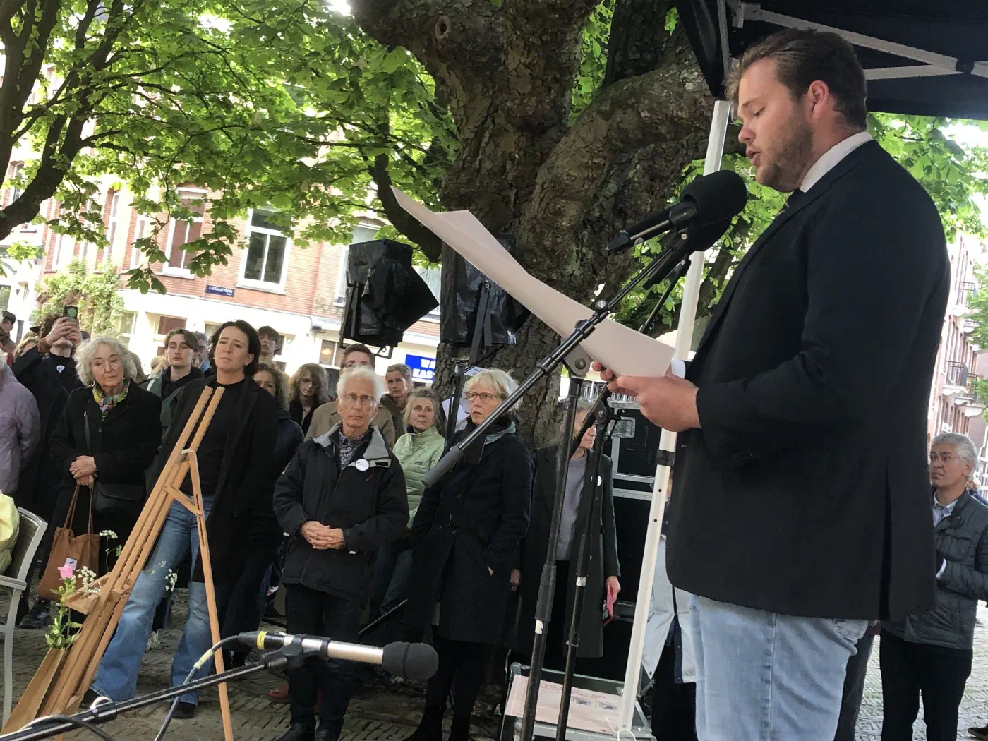 Spreker in donker colbert leest een tekst voor bij de microfoon