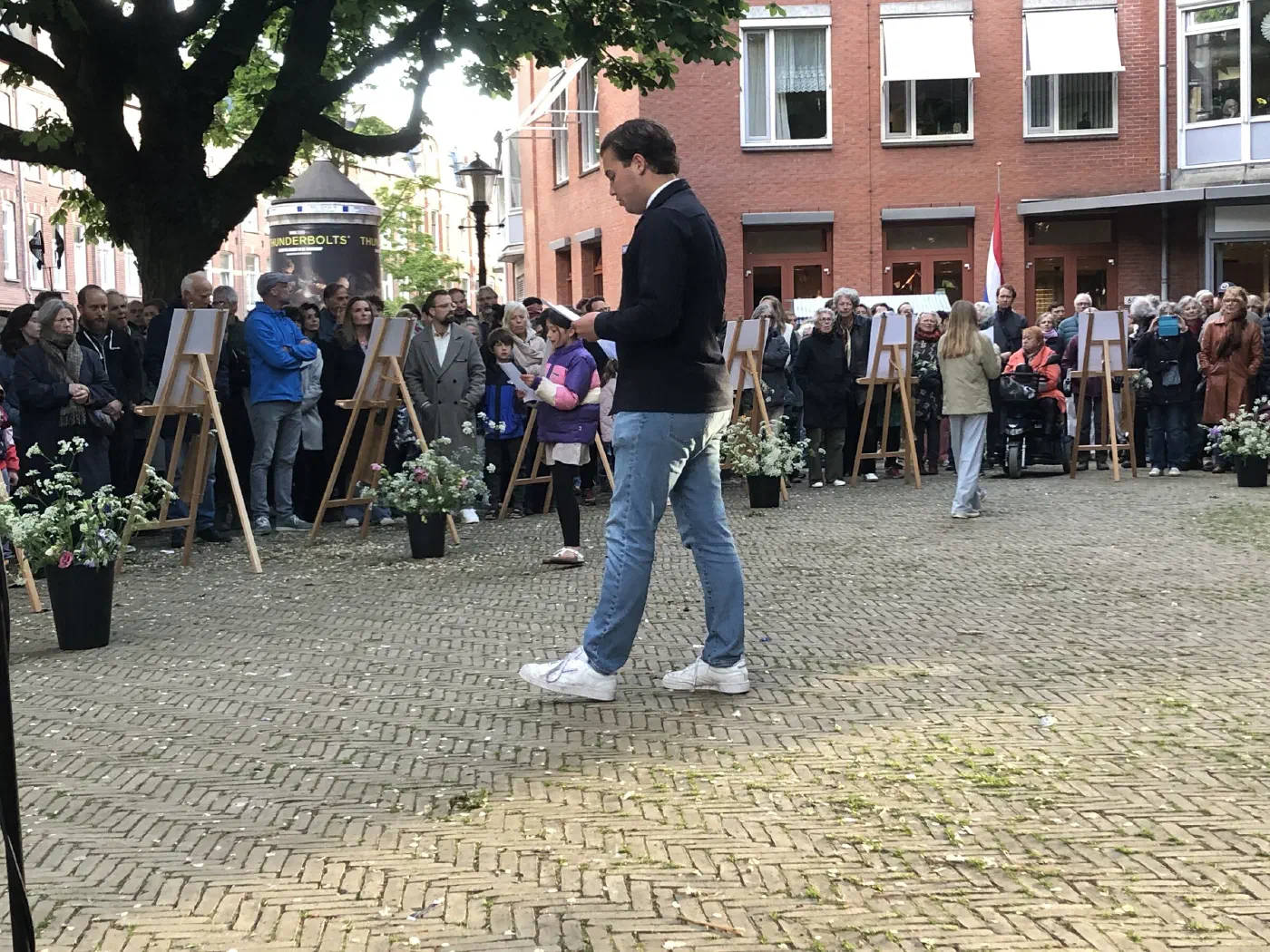 Jongeman loopt over het plein, omringd door publiek en gedenkposters op ezels
