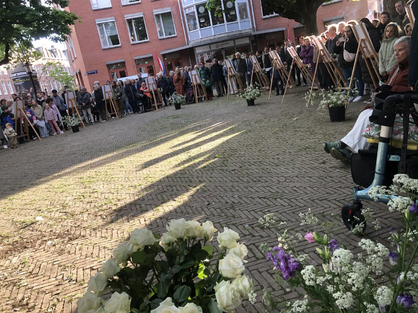 Witte rozen en veldbloemen op de grond, publiek in een kring rond het plein