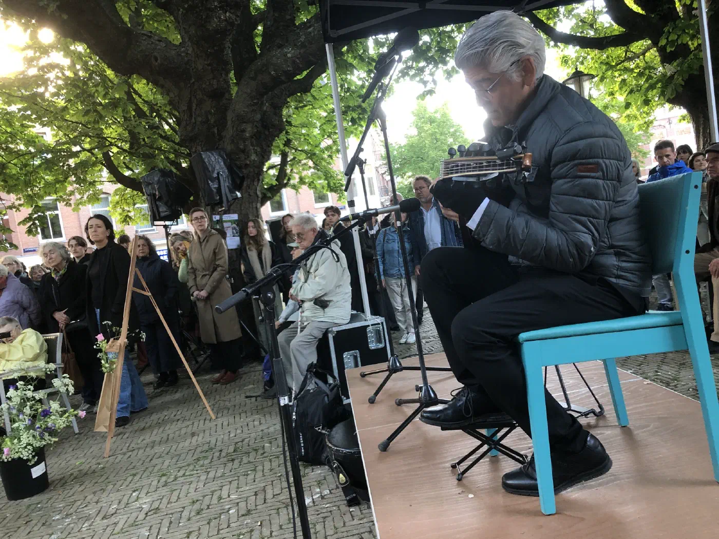Muzikant speelt oed op een turquoise stoel op het podium voor het publiek