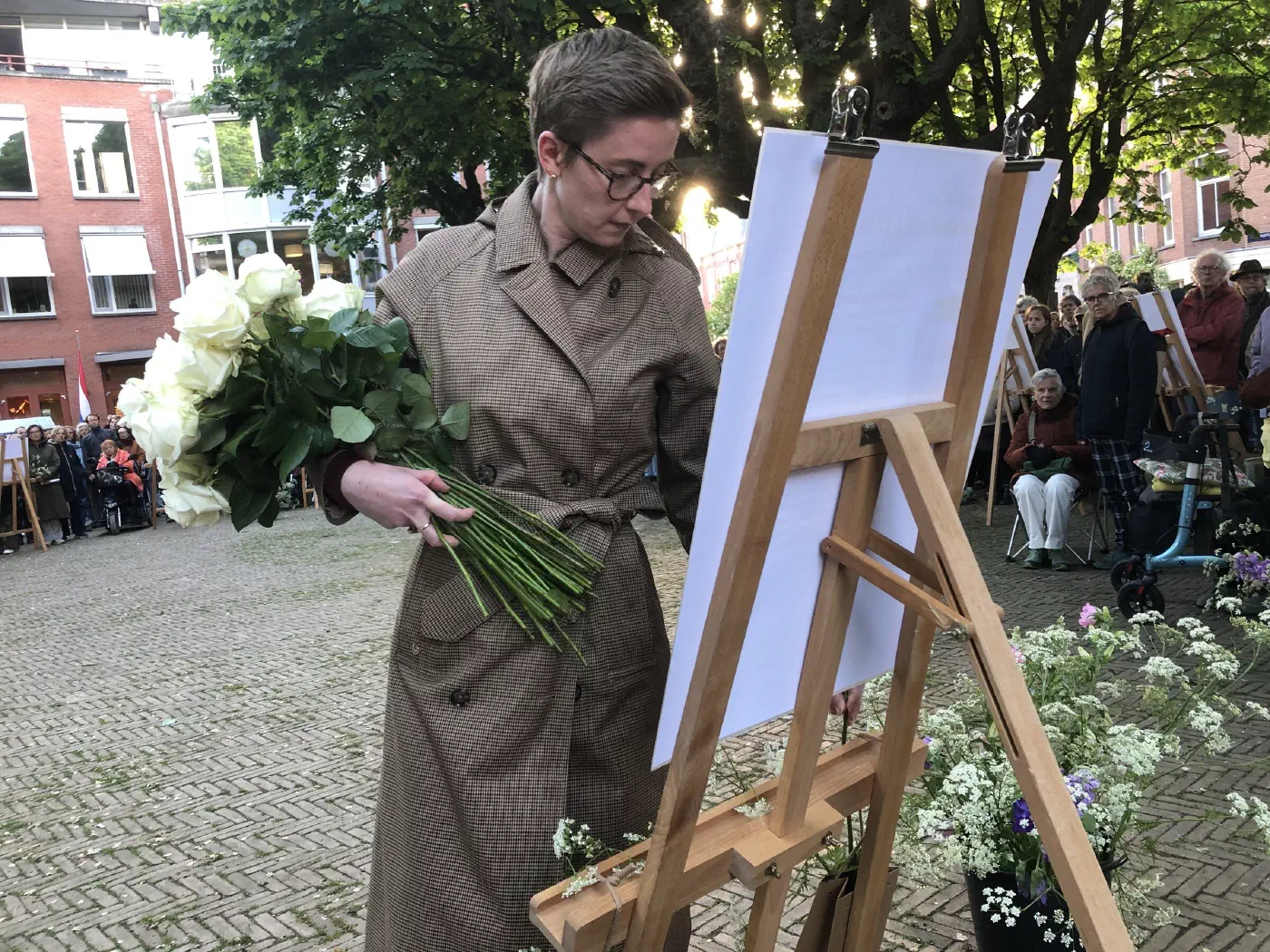 Vrouw met een bos witte rozen legt bloemen bij een gedenkposter