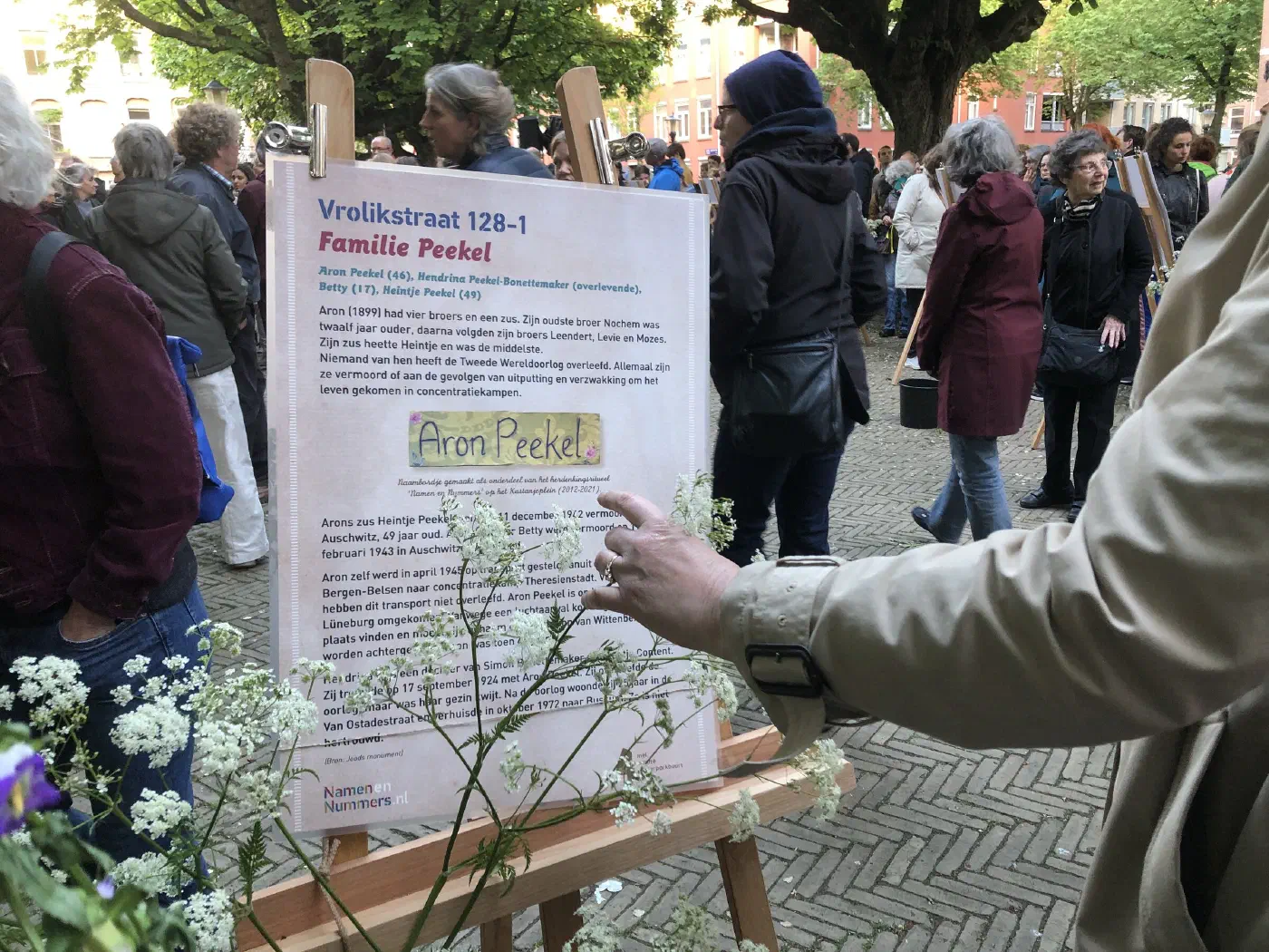 Gedenkposter over familie Peekel, Vrolikstraat 128-1, met bezoekers op de achtergrond