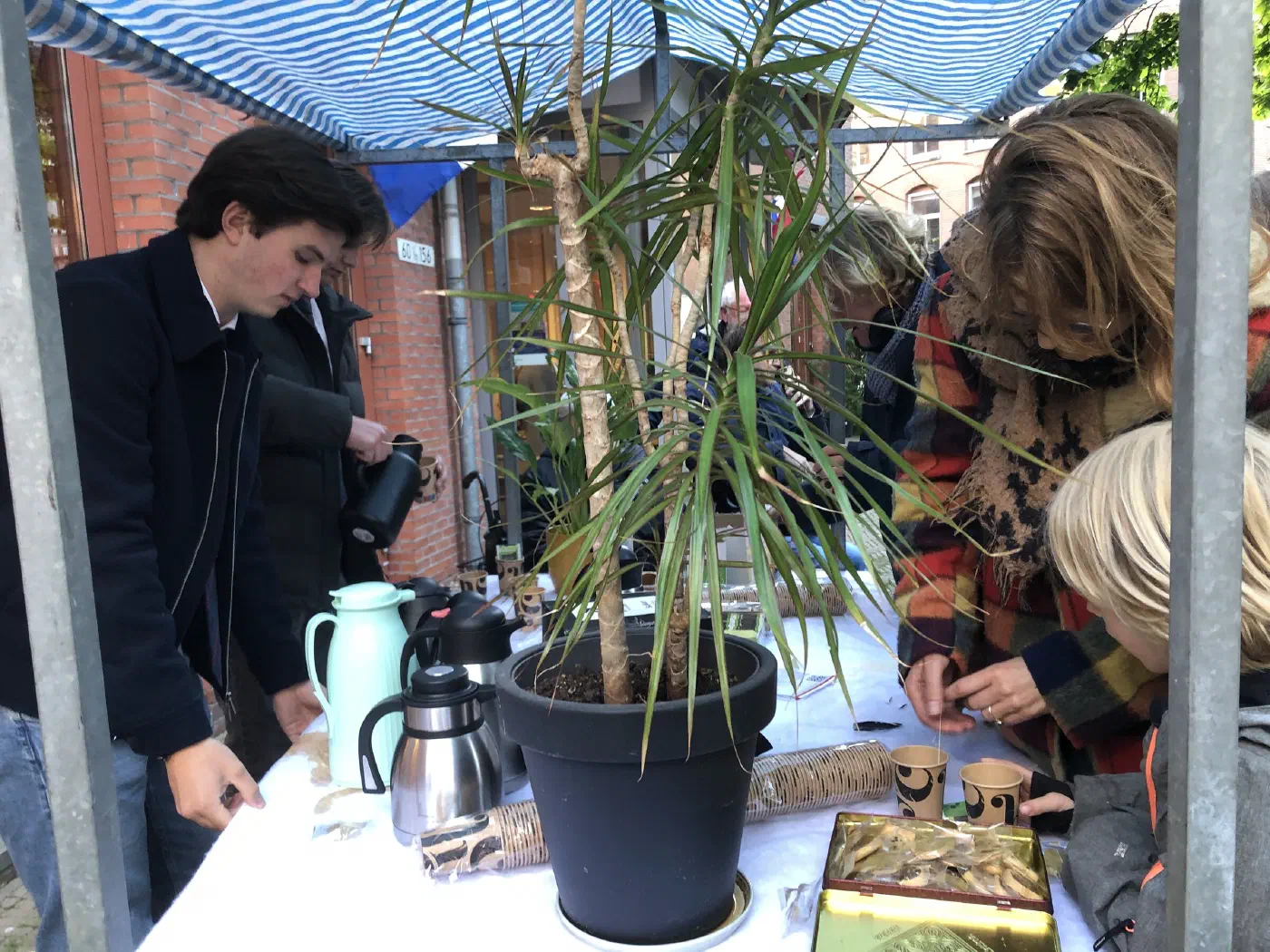 Vrijwilligers schenken koffie en thee aan een tafel onder een luifel