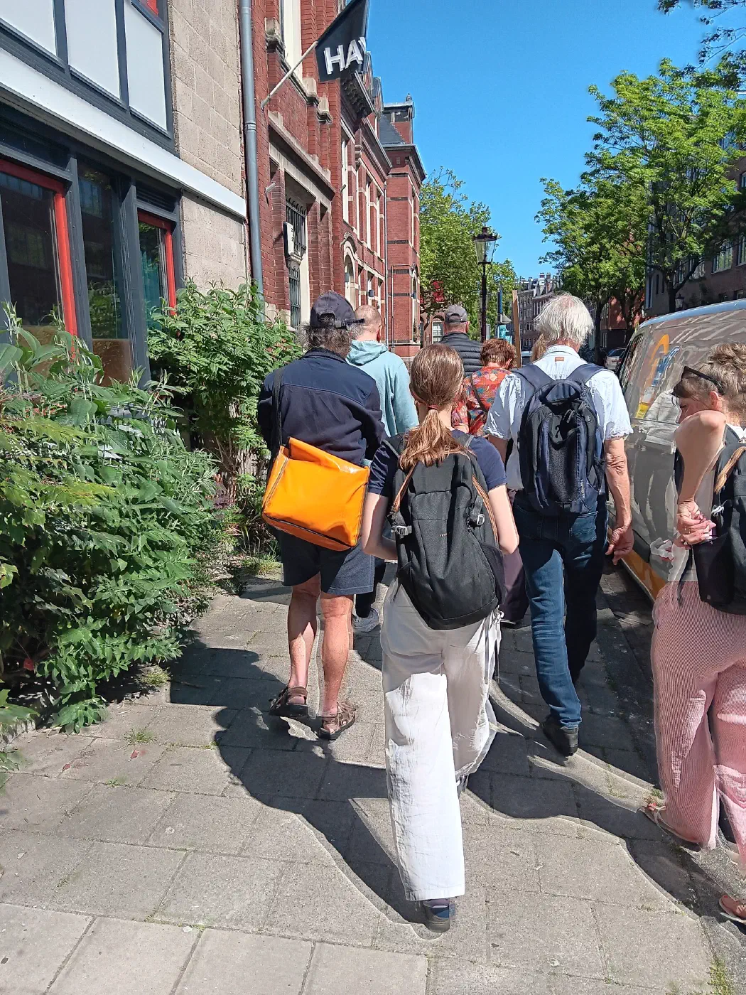 Deelnemers aan de rondleiding lopen in de zon over de stoep