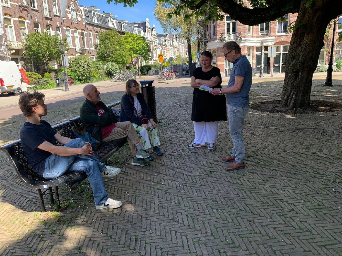 Rondleiders vertellen aan deelnemers op een bankje onder een grote boom