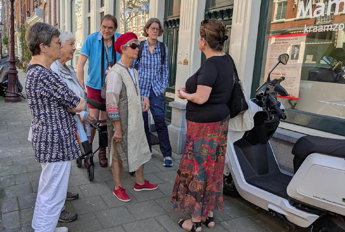 Rondleider in gesprek met deelnemers bij een gedenkposter in een etalage