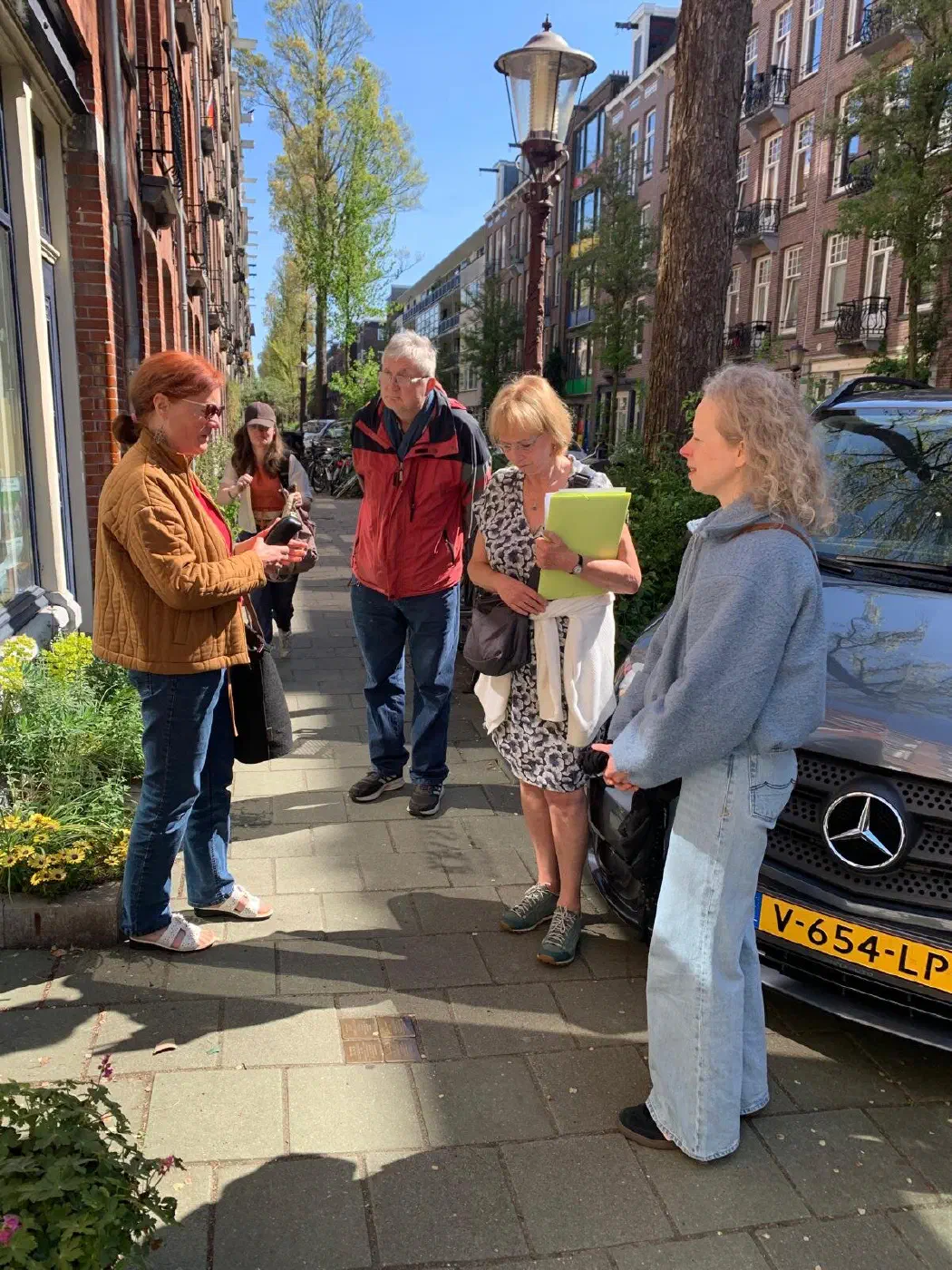 Kleine groep luistert naar een rondleider met een groene map op de stoep