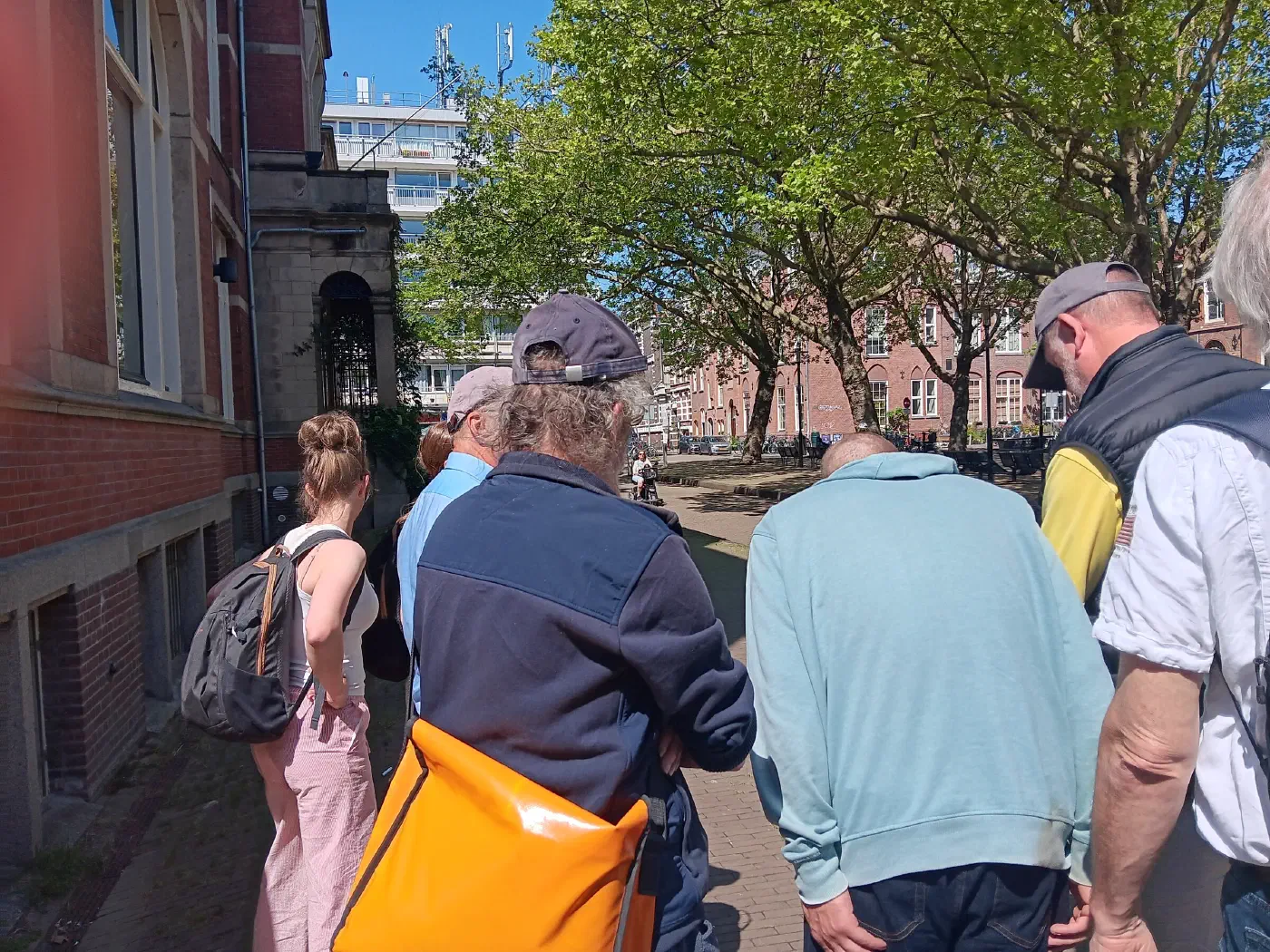 Deelnemers kijken naar de grond tijdens de rondleiding in een zonnige straat