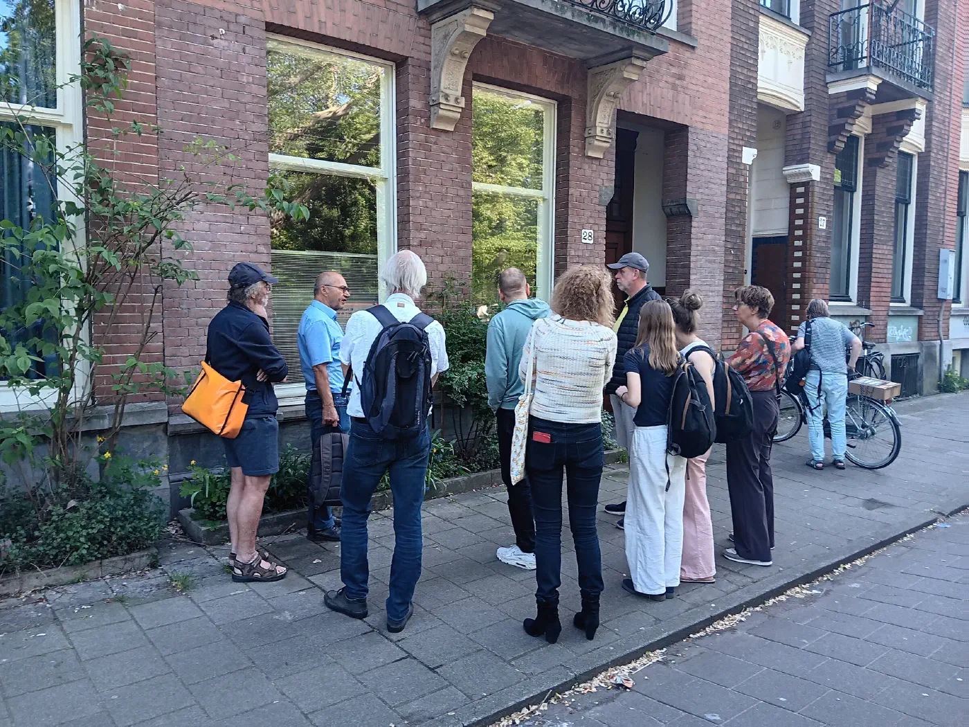 Grote groep deelnemers staat stil voor een herenhuis tijdens de rondleiding