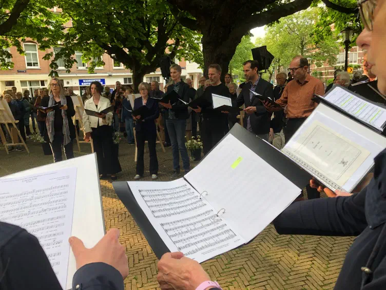 Koorleden met bladmuziek zingen in een kring tussen het publiek op het Kastanjeplein