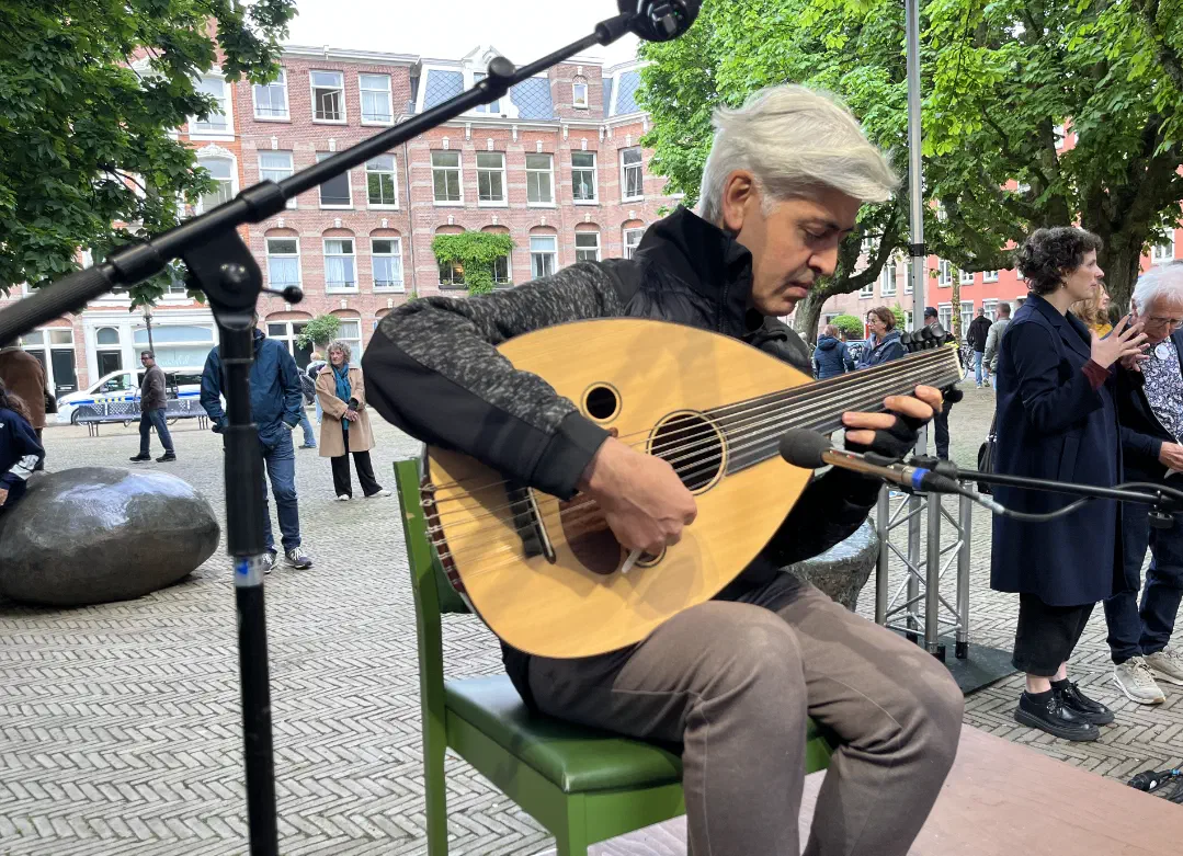 Muzikant met grijs haar speelt oed op een groene stoel op het plein