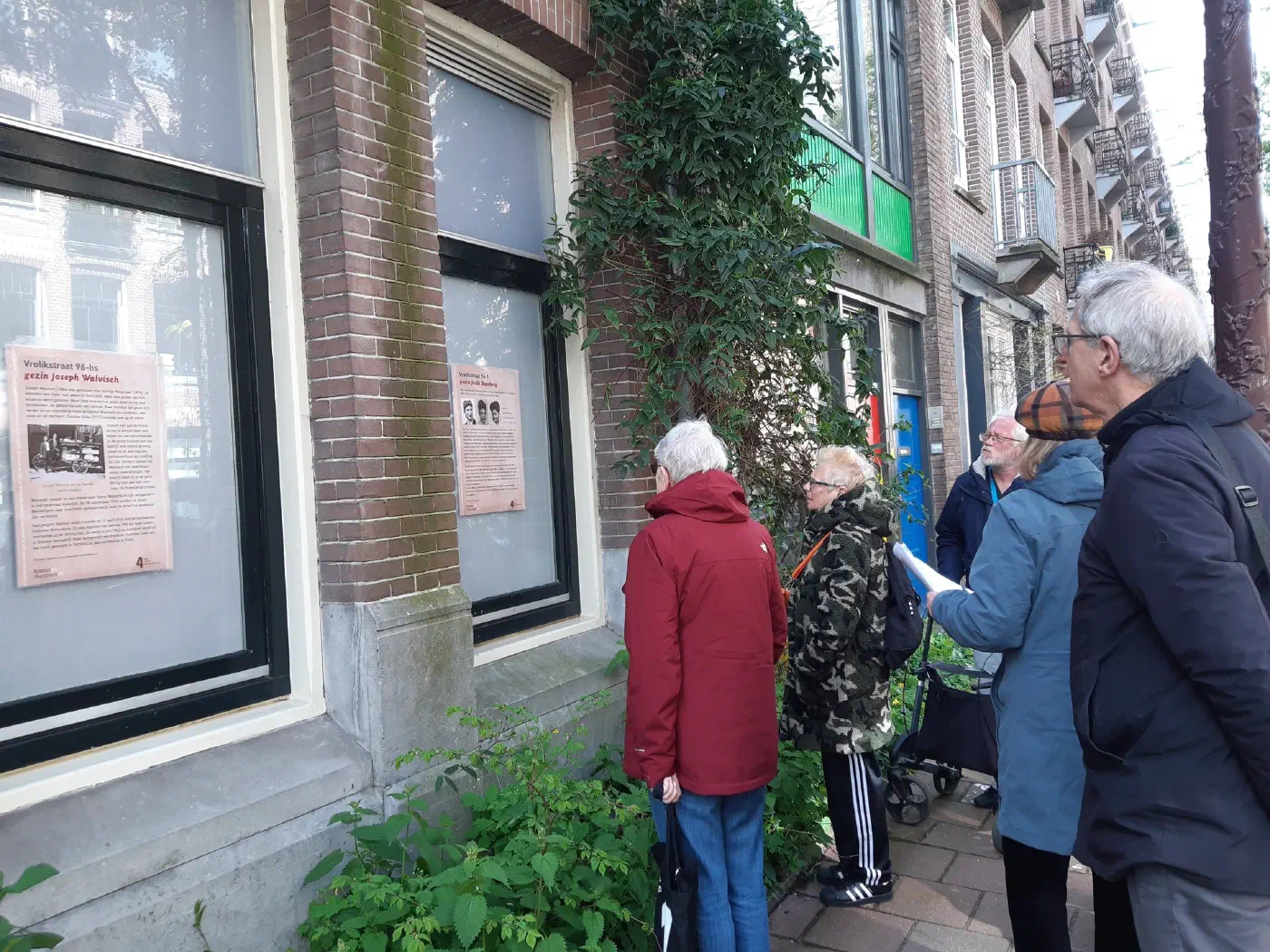 Wandelaars lezen de gedenkposters op Vrolikstraat 96, waaronder die voor gezin Joseph Walvisch