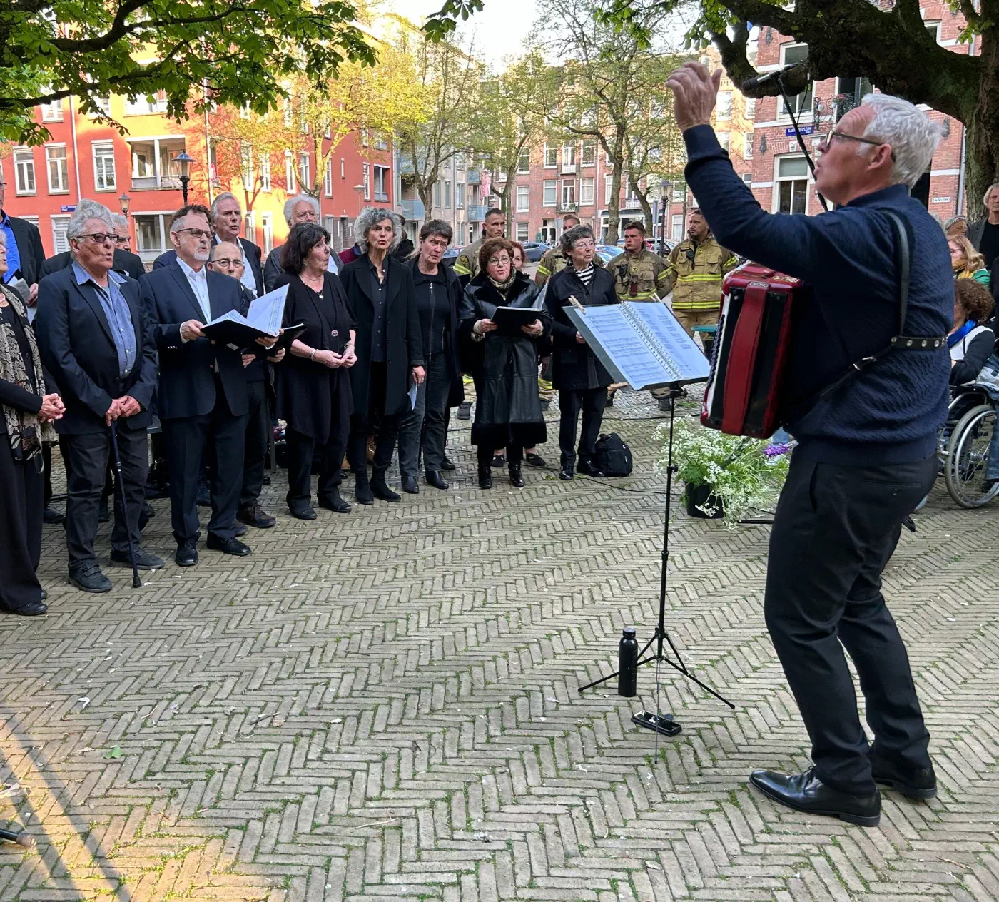 Dirigent met accordeon leidt het koor op het Kastanjeplein
