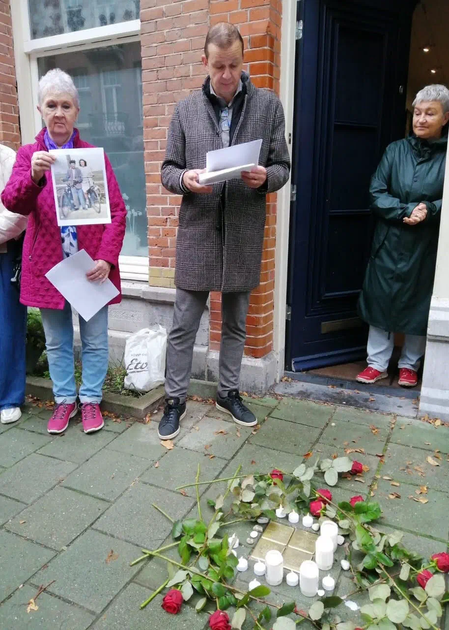 Man leest toespraak voor bij de nieuwe struikelstenen, omringd door kaarsjes en rozen