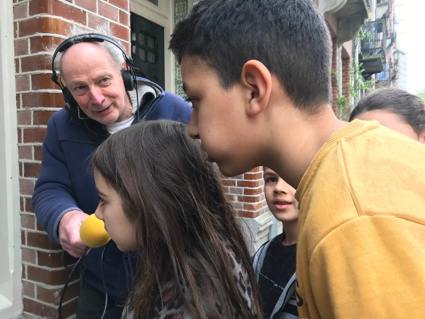 Man met koptelefoon en microfoon neemt kinderen op die een gedenkposter voorlezen